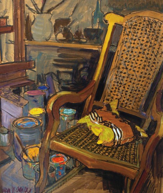 Silla de mimbre con un cojín amarillo, rodeada de latas de pintura y objetos variados.