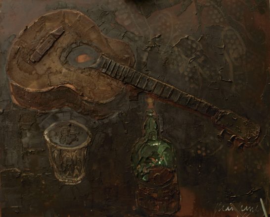 Guitarra de madera sobre una superficie oscura junto a un vaso y una botella verde.